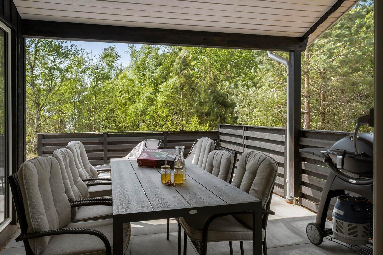 Terrasse mit Esstisch, Stühlen und Grill. Blick in den Wald.