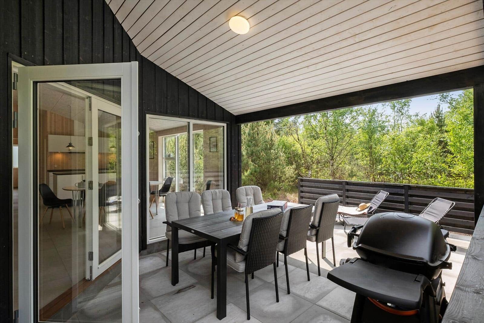 Terrasse mit Esstisch, Grill und Sitzgelegenheiten. Blick in die Küche und auf grüne Umgebung.