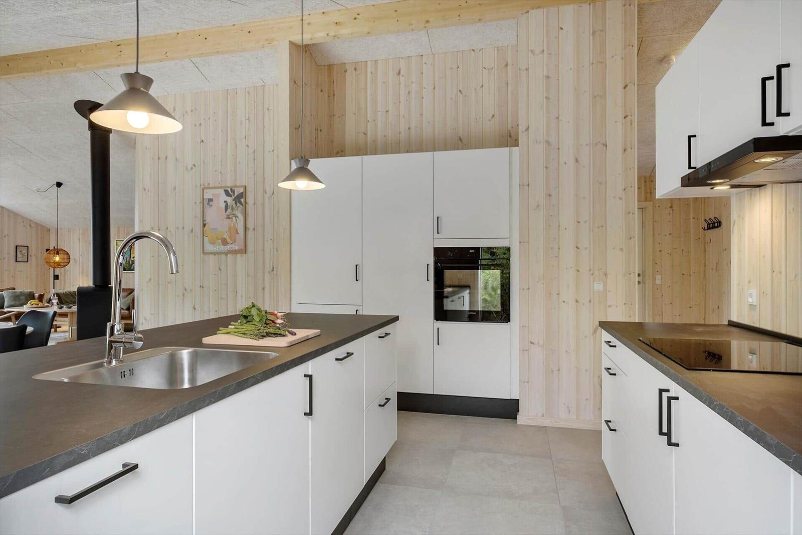 Moderne Küche mit weißen Schränken, dunklem Arbeitsplatz und Holzwandverkleidung.