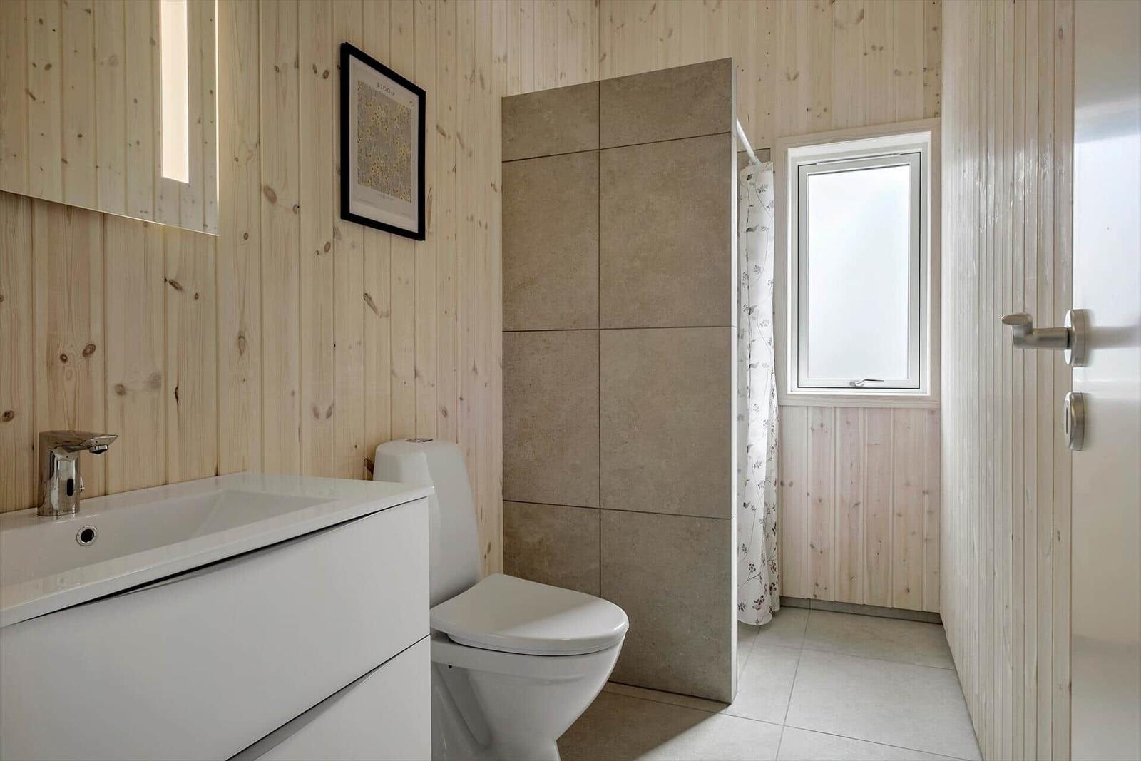 Badezimmer mit Holzwand, Toilette, Waschbecken und Dusche