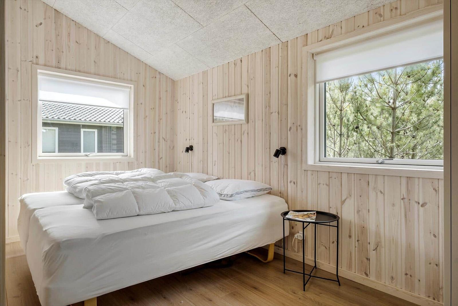 Schlafzimmer mit Holzwand, Bett und Fenstern.