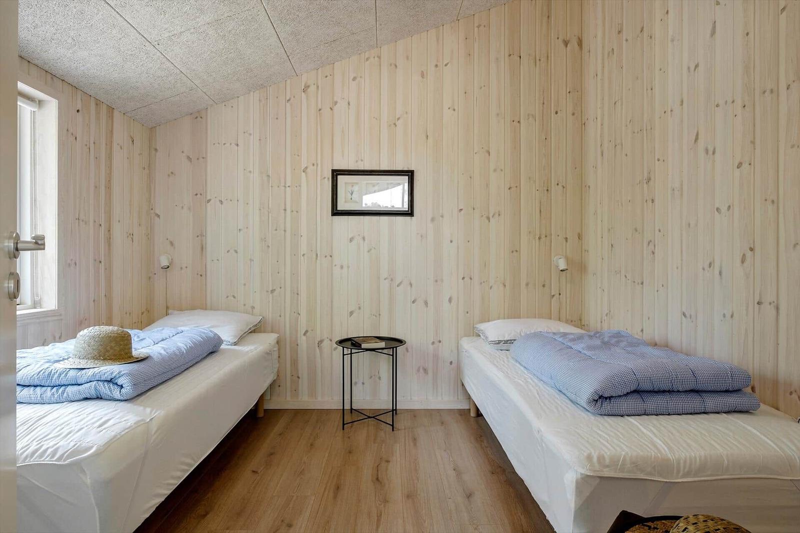 Zwei Betten mit blauen Decken, Holzwand und kleiner Tisch.