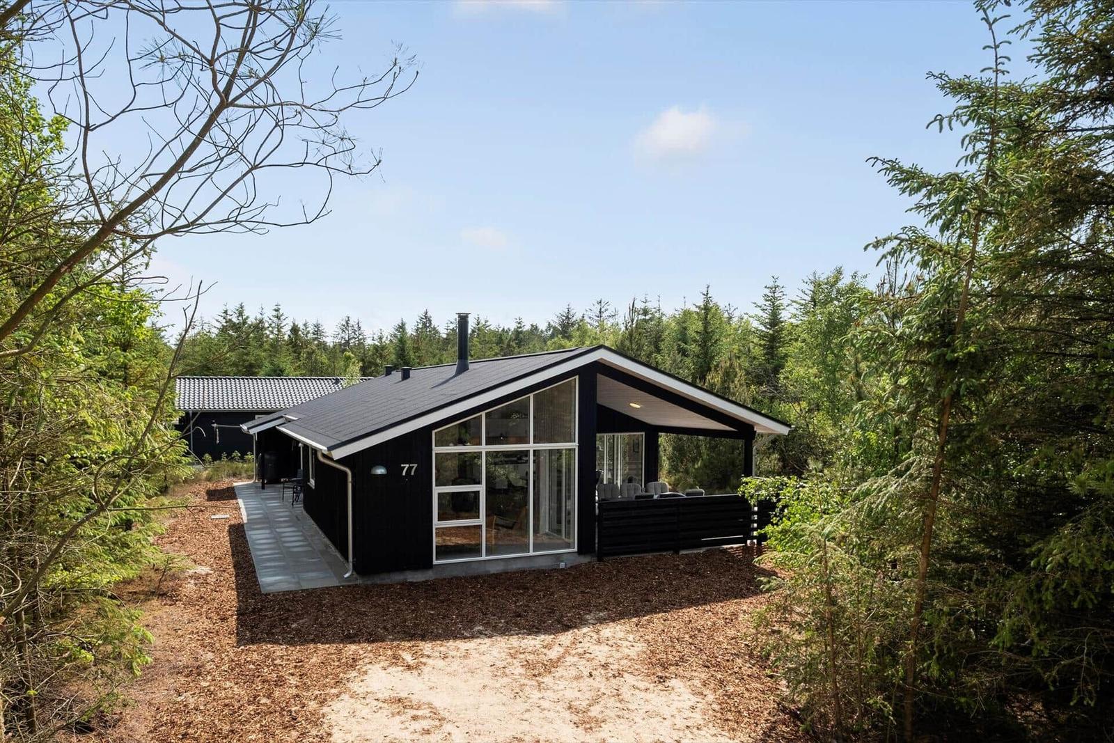 Moderne schwarze Hütte mit großem Fenster und Terrasse im Wald.