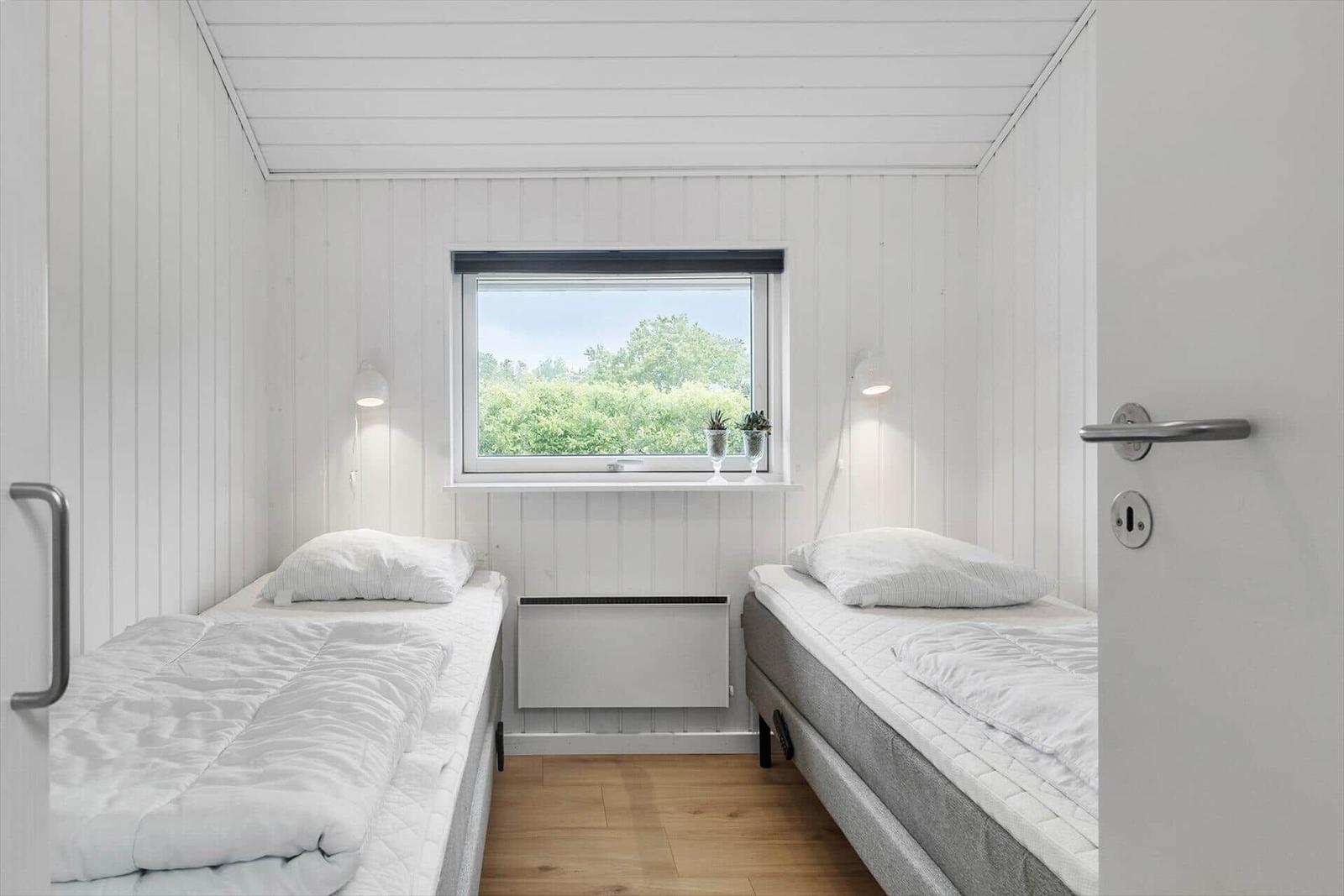 Zwei Betten, Fenster mit Blick auf Grün, weiße Wände und Holzboden.
