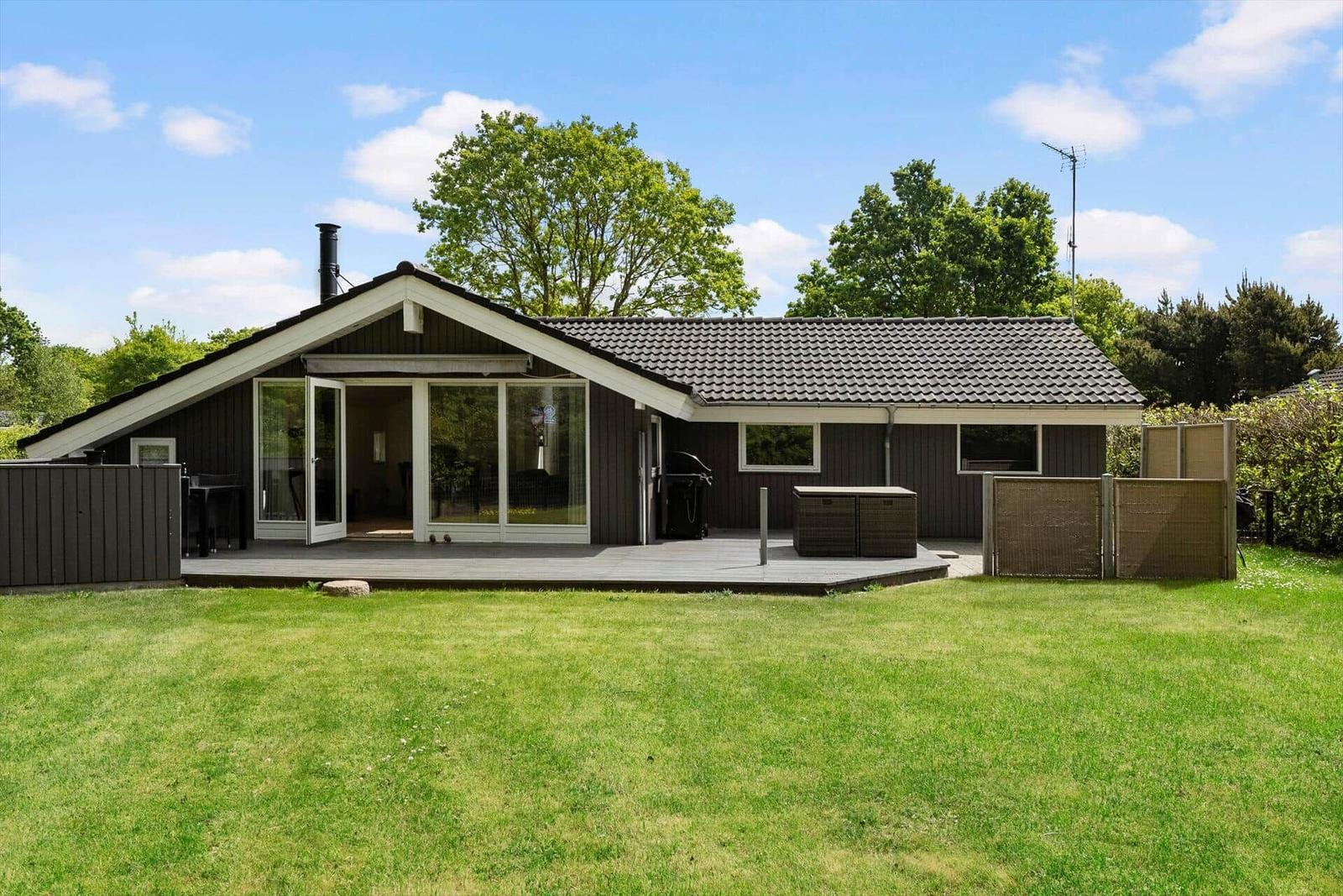 Ein Haus mit Terrasse, Grill und Garten unter blauem Himmel.