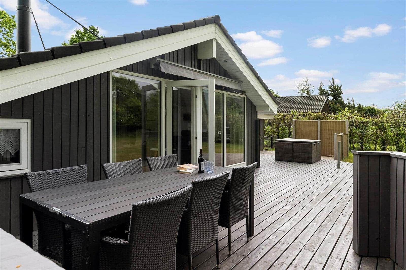 Terrasse mit Tisch und Stühlen, Anschluss an Wohnraum, Gartenbereich mit Sicht auf Bäume.