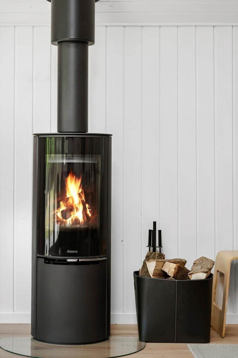 Moderne Kaminfeuerstelle mit Holzstapel und Glasfront vor weißer Wand.