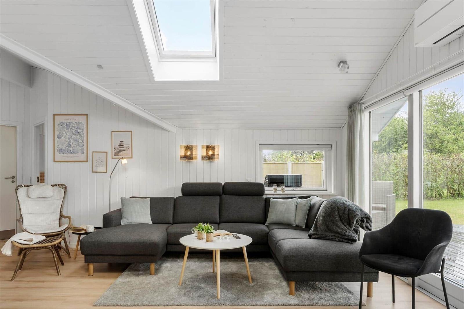 Wohnzimmer mit grauem Sofa, runder Tisch und großen Fenstern.