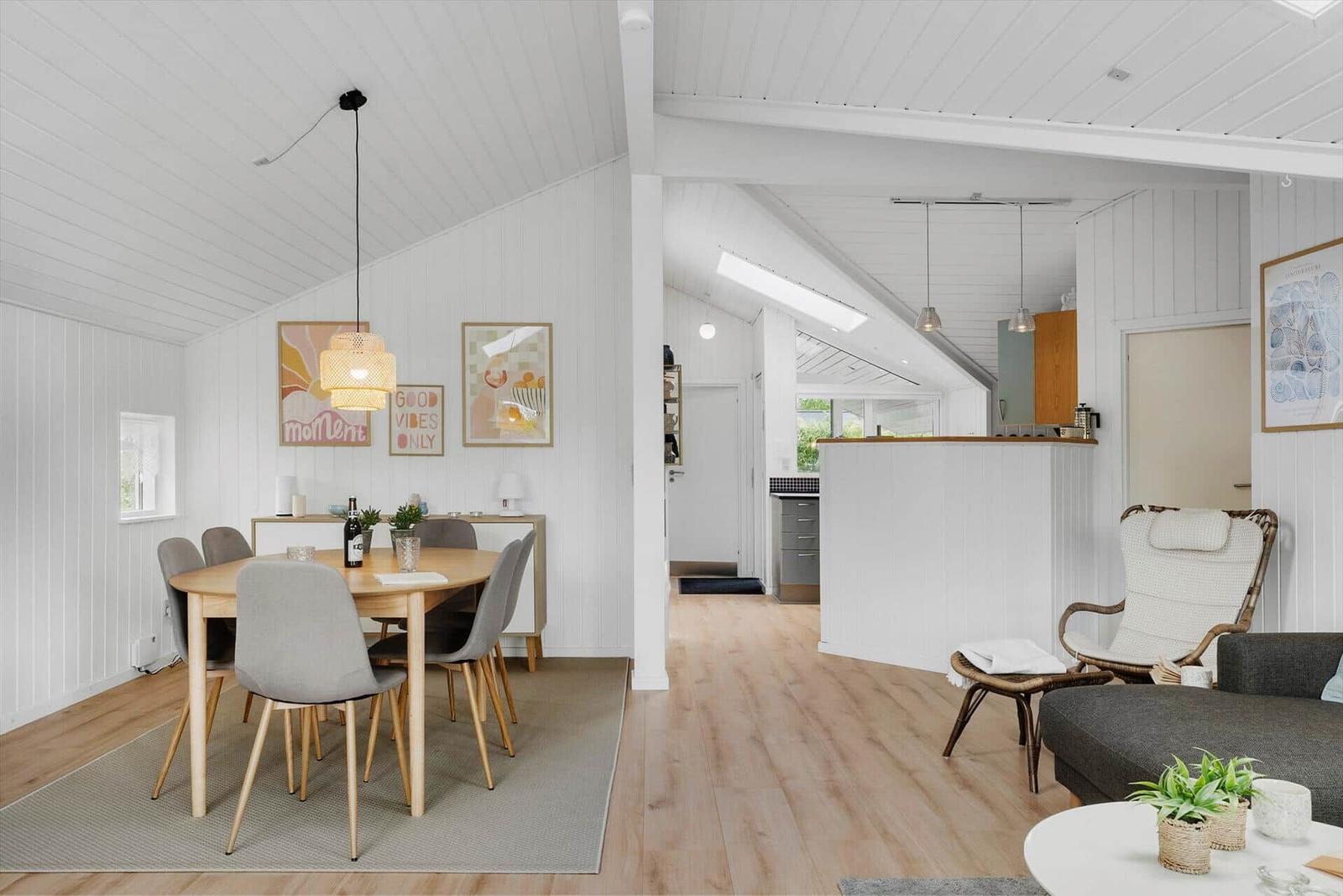 Essbereich mit Tisch und Stühlen, Wohnbereich mit Sofa und Sessel, Küche im Hintergrund.