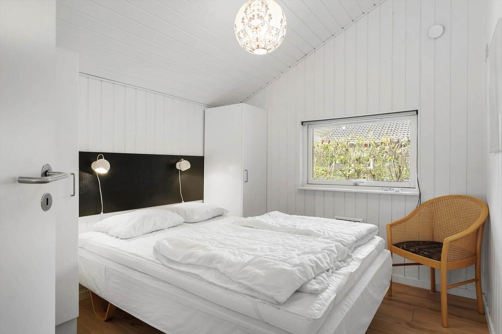 Schlafzimmer mit Bett, Stuhl und Fenster. Weiße Wände und Holzboden.