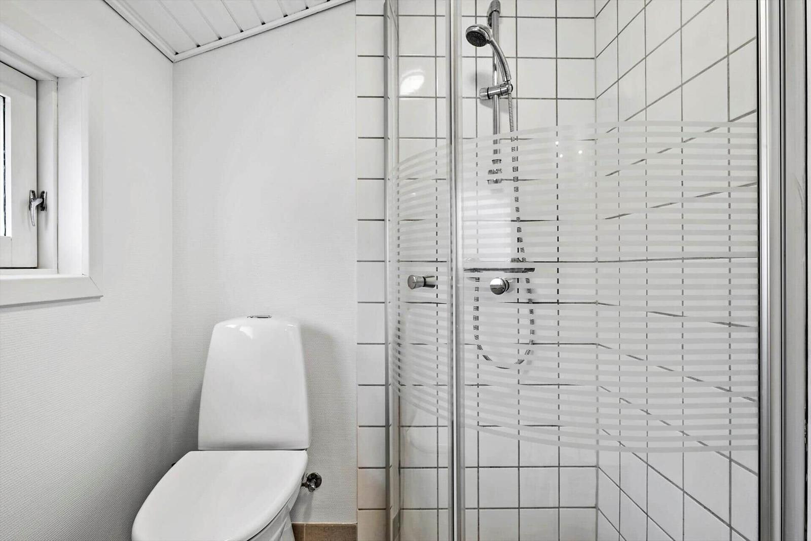 Bad mit Dusche und Toilette, weiße Fliesen und Fenster