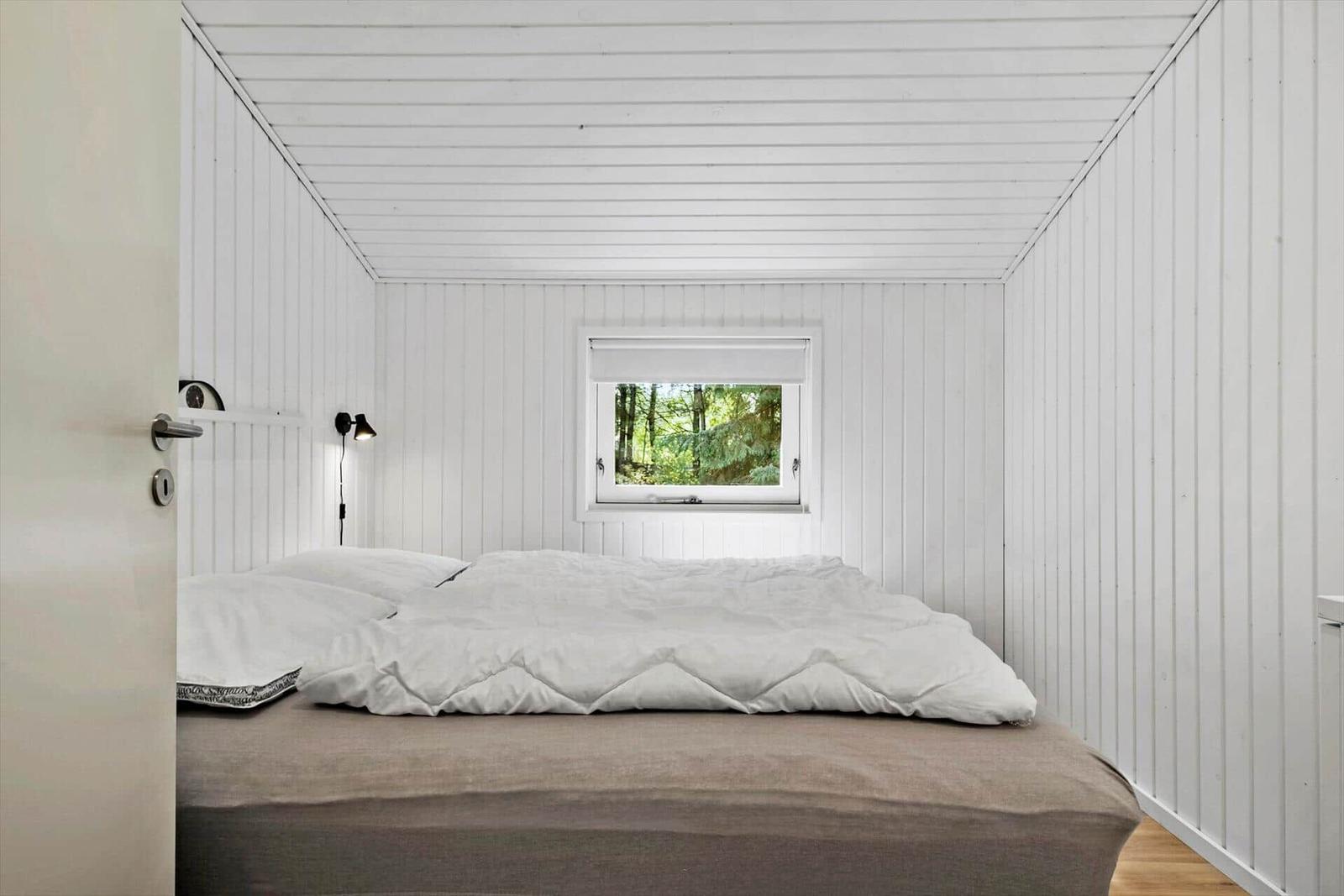 Schlafzimmer mit weißem Bett und Fenster zum Wald.