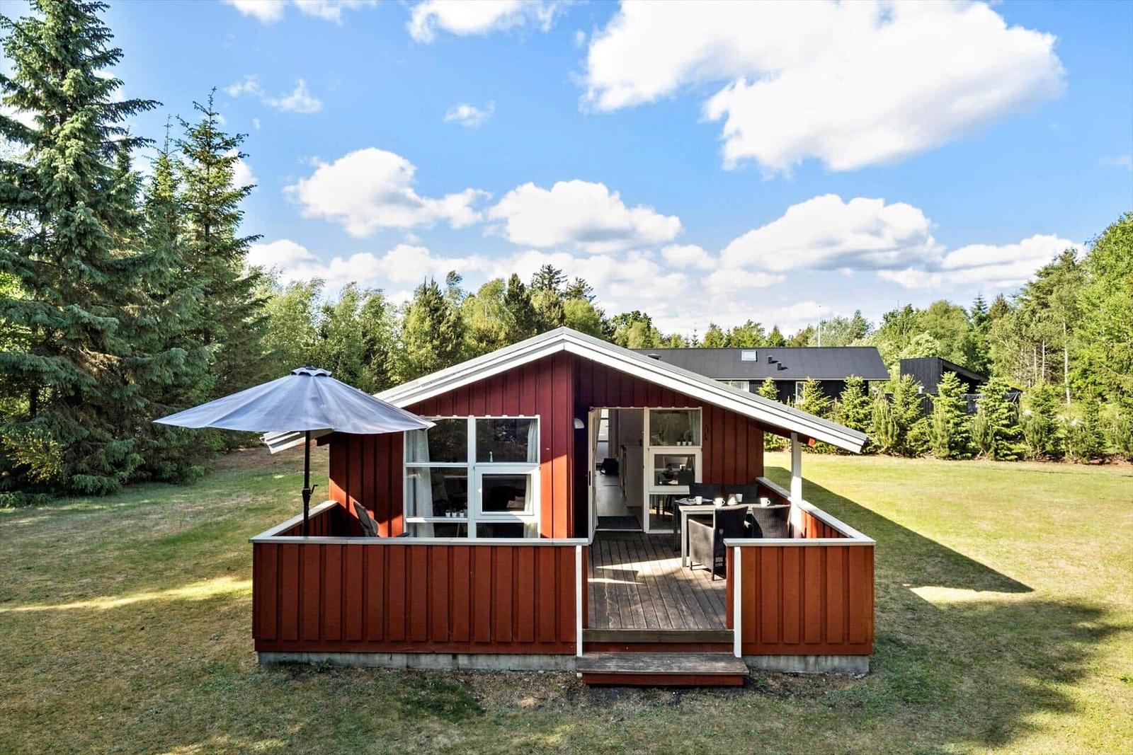 Roter Holzhaus mit Terrasse und Garten unter blauem Himmel.