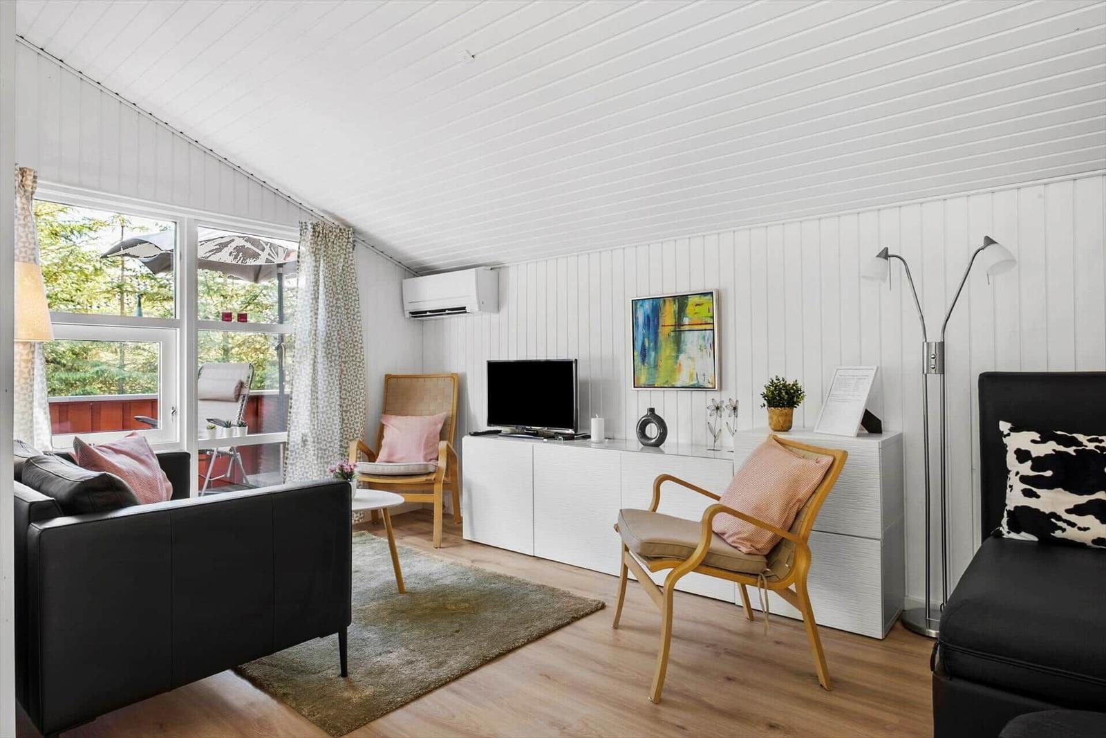 Wohnzimmer mit schwarzen Sofas, Holzstühlen und Fernseher an weißer Wand.