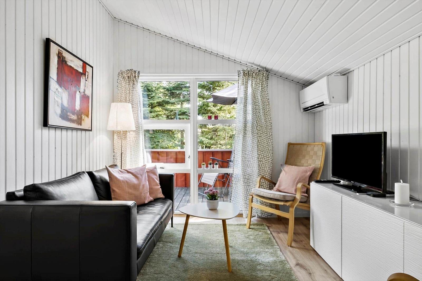 Wohnzimmer mit Sofa, Stuhl und TV. Blick auf Balkon mit Garten.