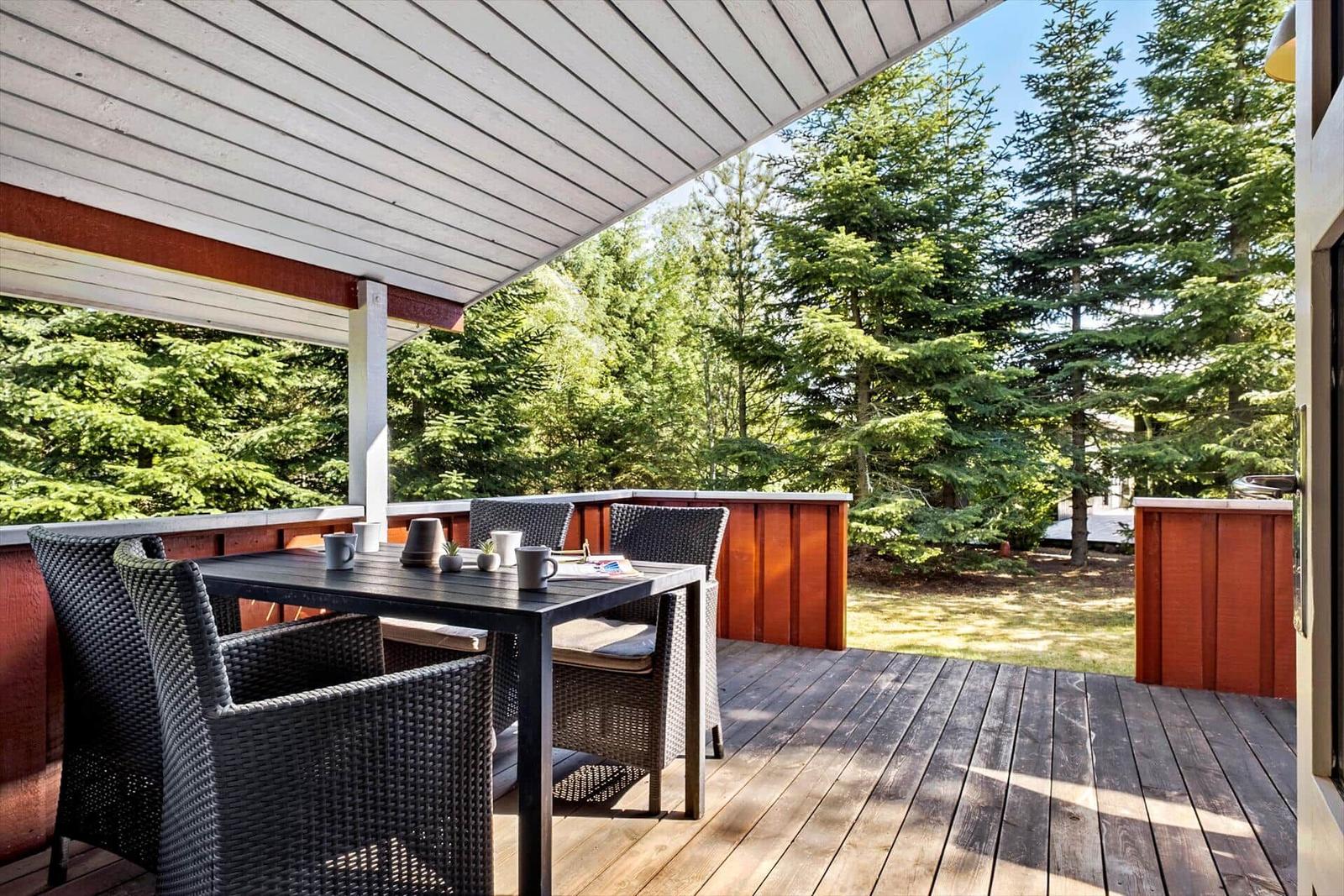 Terrasse mit Tisch und Stühlen, umgeben von Bäumen und Holzgeländern.