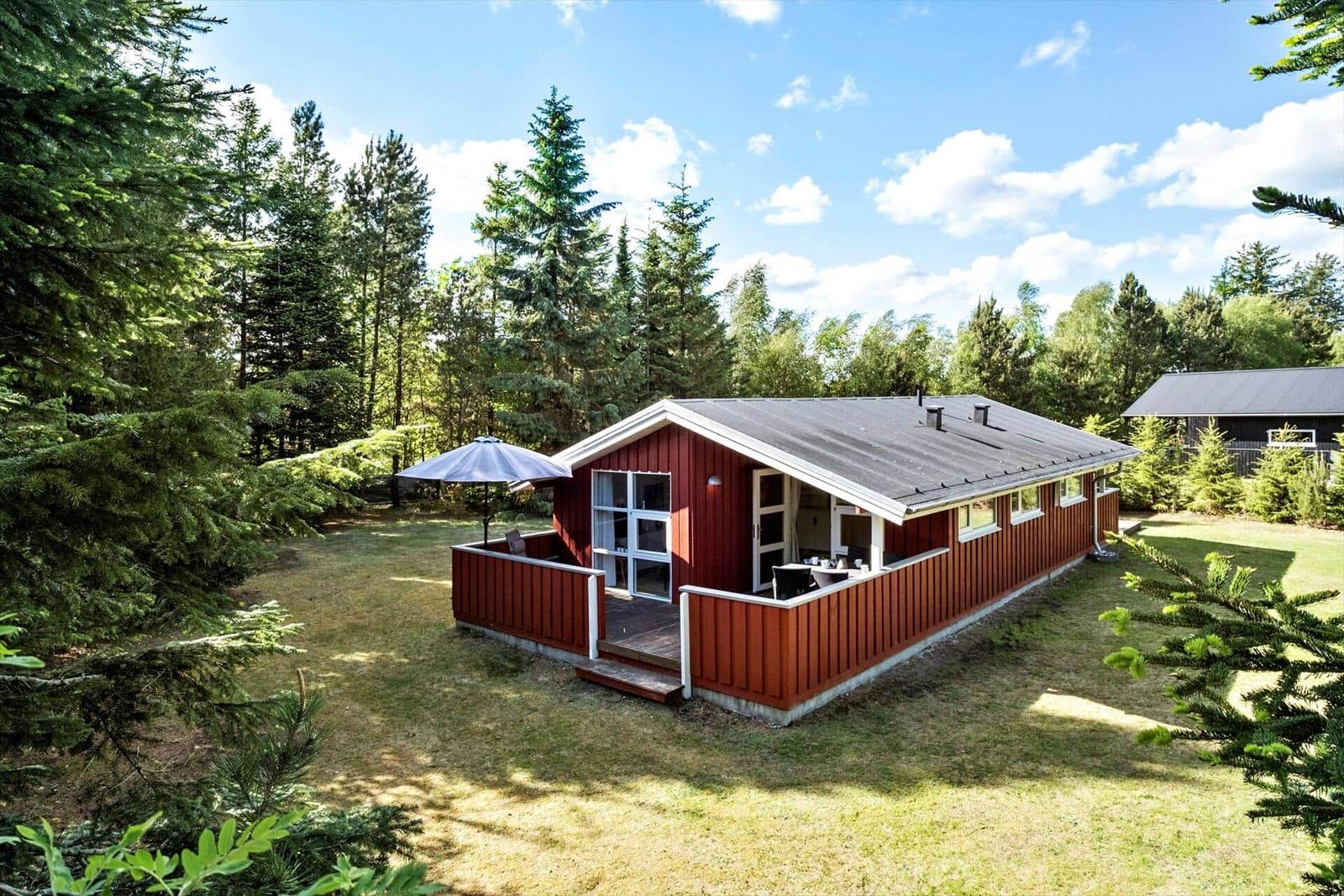 Rotes Holzhaus mit Terrasse und Garten in einem Waldgebiet.