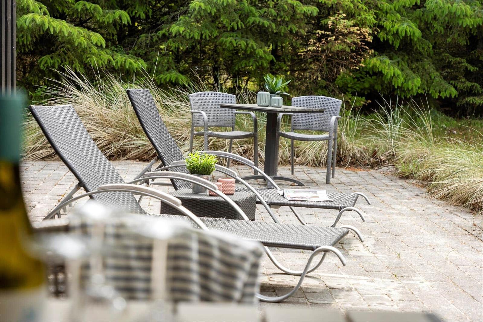 Terrasse mit Liegestühlen, Tisch und Stühlen, umgeben von Gräsern und Bäumen.