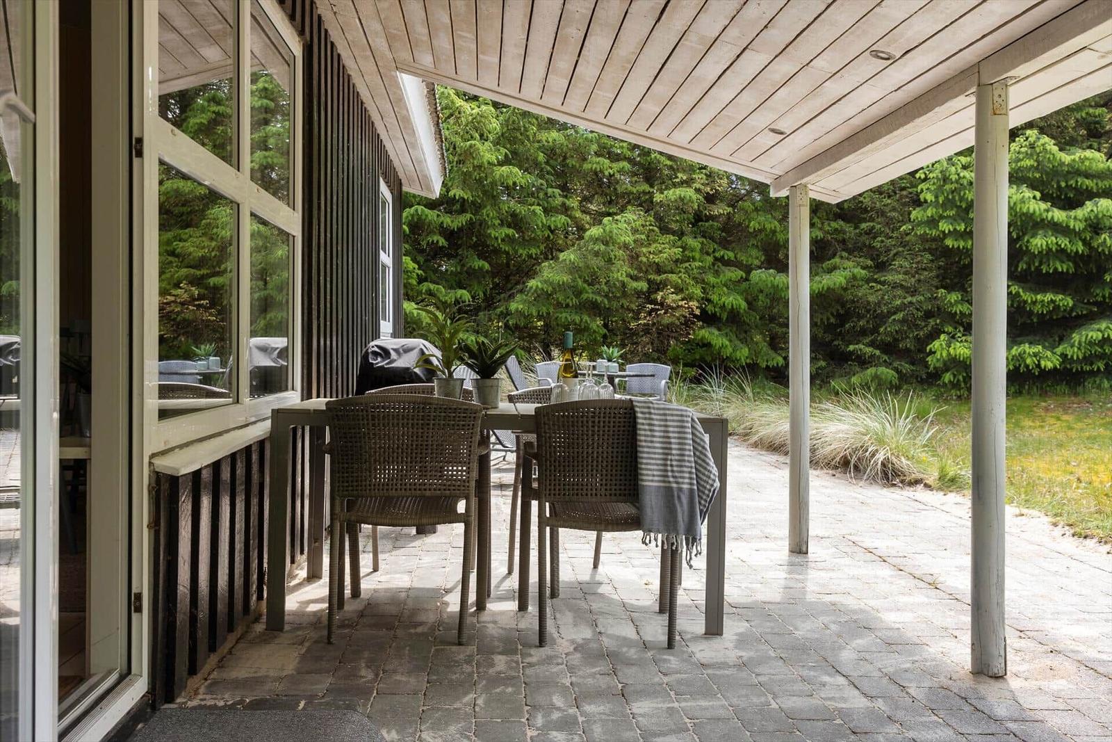 Terrasse mit Tisch und Stühlen, umgeben von Bäumen und Pflanzen.