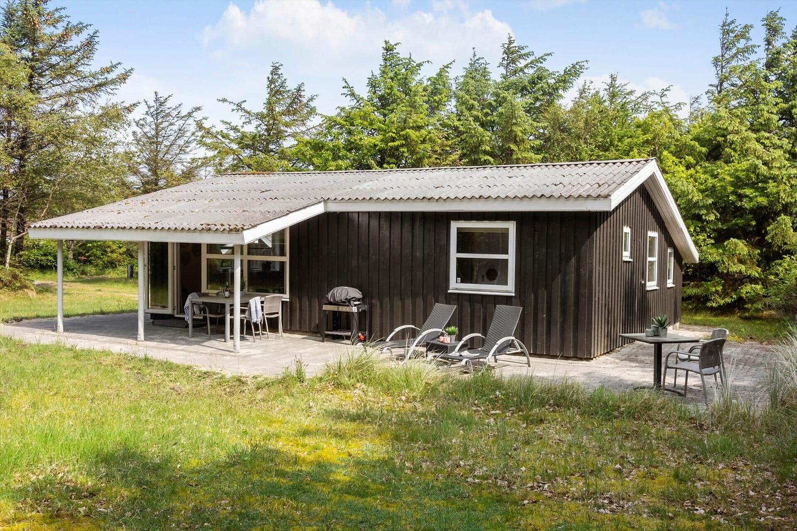 Ein kleines Haus mit Terrasse, Liegestühlen und Grillplatz im Grünen.