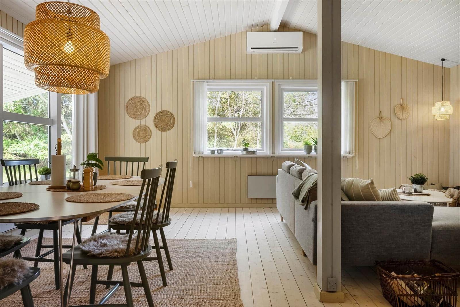 Essbereich mit Tisch und Stühlen, Wohnbereich mit Sofa, Holzwände und Fenster.