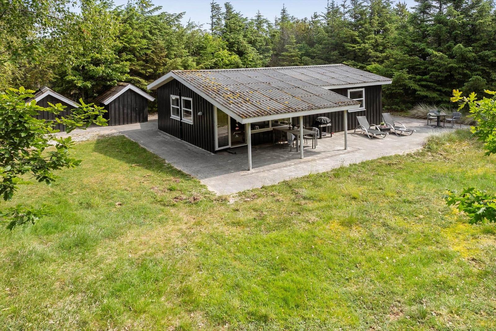 Hütte mit Terrasse, Grill und Liegen im Grünen.