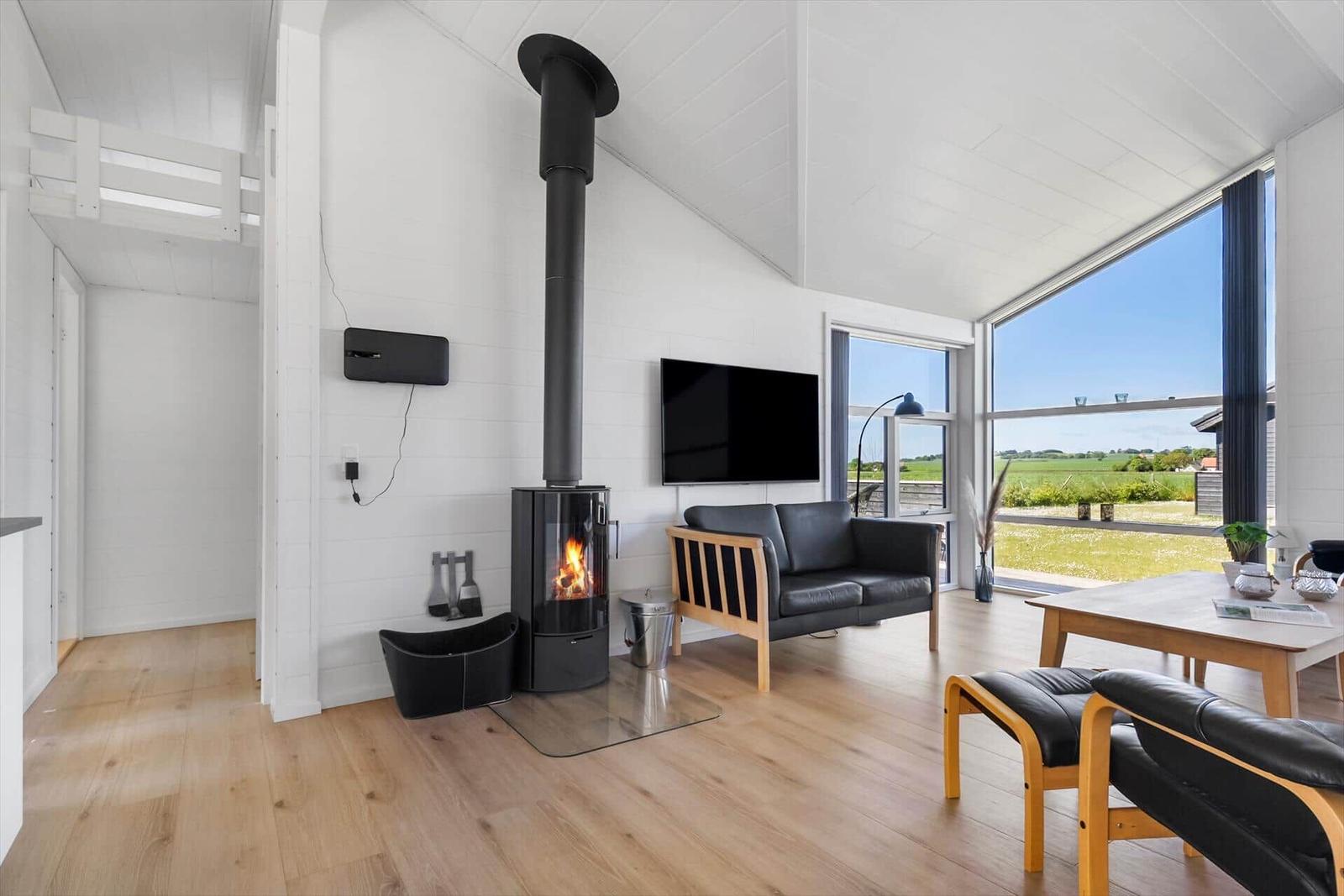 Wohnraum mit Kamin, Sofa und großem Fenster mit Blick auf Felder.
