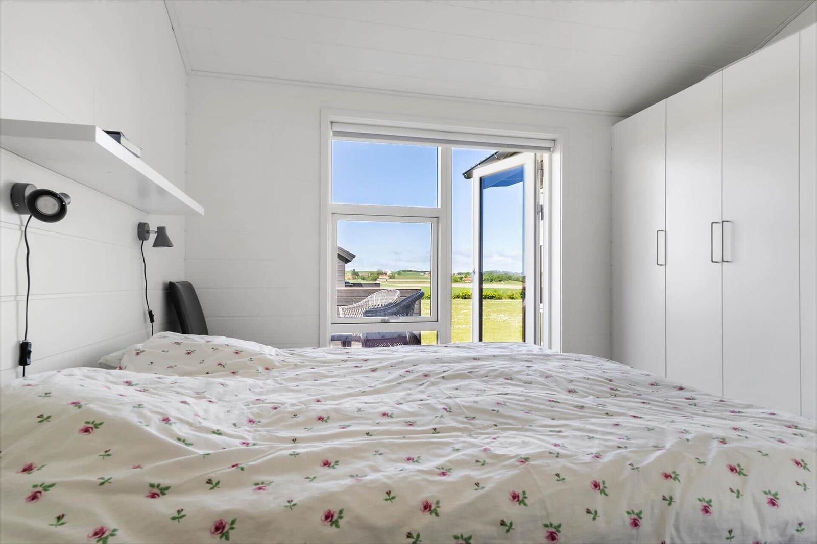Schlafzimmer mit Blick auf Terrasse und Grünfläche. Weiße Wände, Bett mit Blumenbezug.