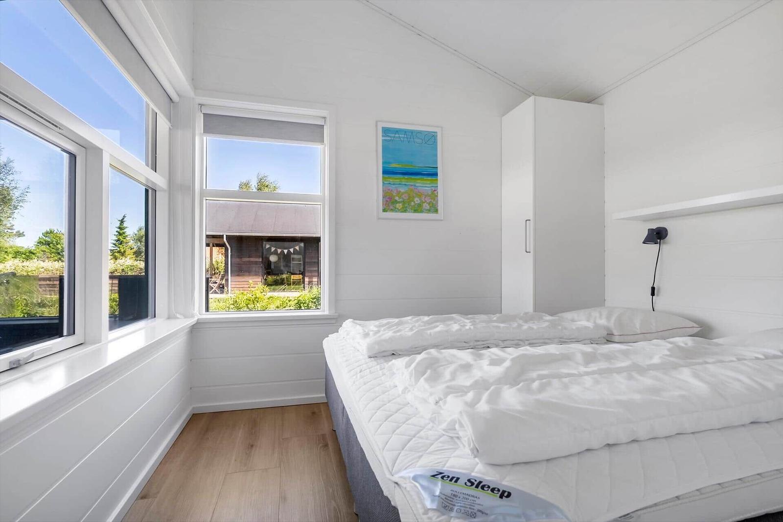 Schlafzimmer mit weißem Bett, Fenstern und Holzboden.