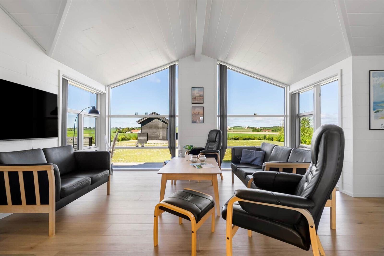 Wohnzimmer mit schwarzen Ledersofas, Holztisch und großem Fensterblick auf die Landschaft.