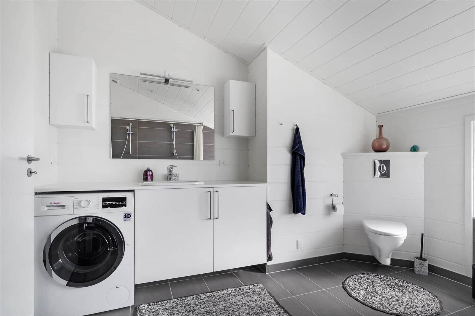 Badezimmer mit Waschmaschine, Spiegel und Toilette.