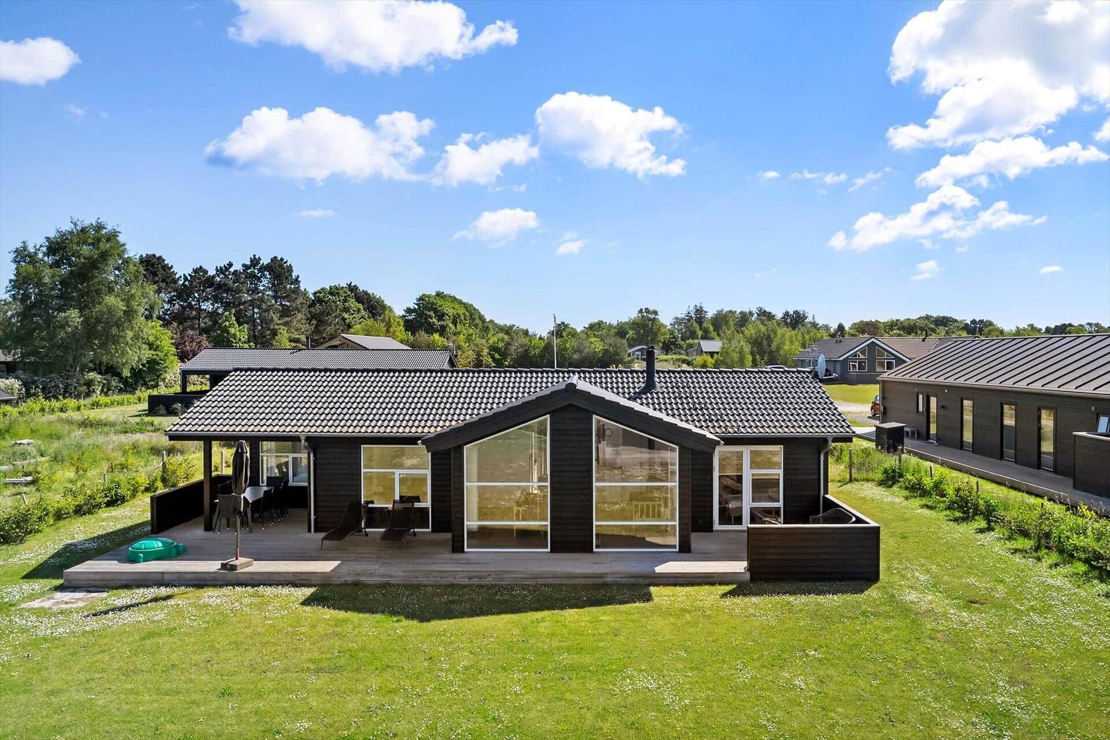 Modernes Haus mit großem Garten und Terrasse unter blauem Himmel.