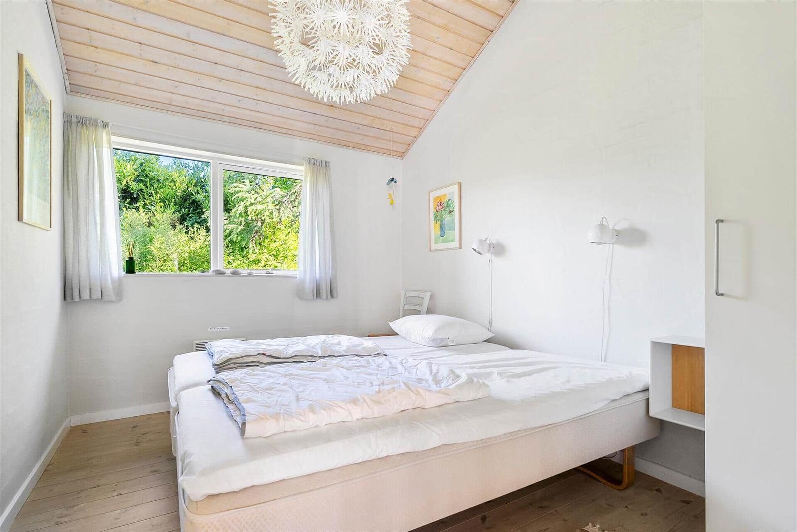 Schlafzimmer mit Doppelbett, Holzboden und Fenster mit Blick auf Grün.