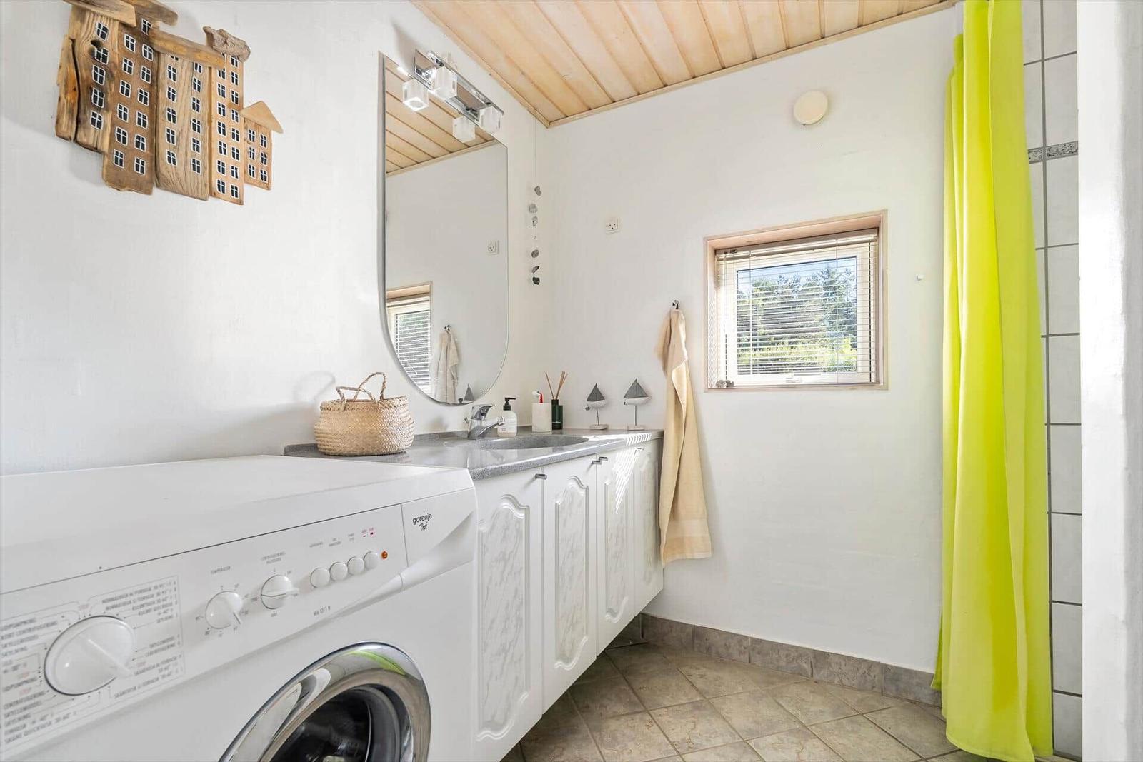 Badezimmer mit Waschmaschine, Spiegelschrank und grünem Duschvorhang.