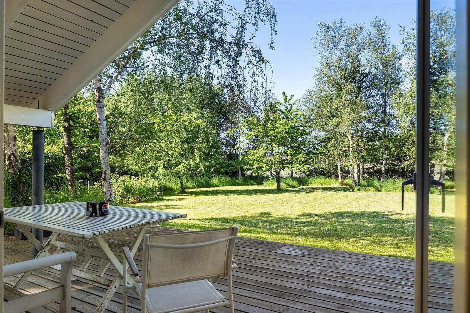 Terrasse mit Tisch und Stühlen, Blick auf grünen Garten und Bäume.