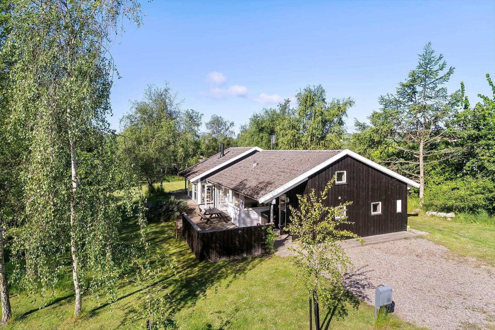 Ein Haus mit dunkler Fassade und weißem Dachrand, umgeben von Bäumen und Gras.
