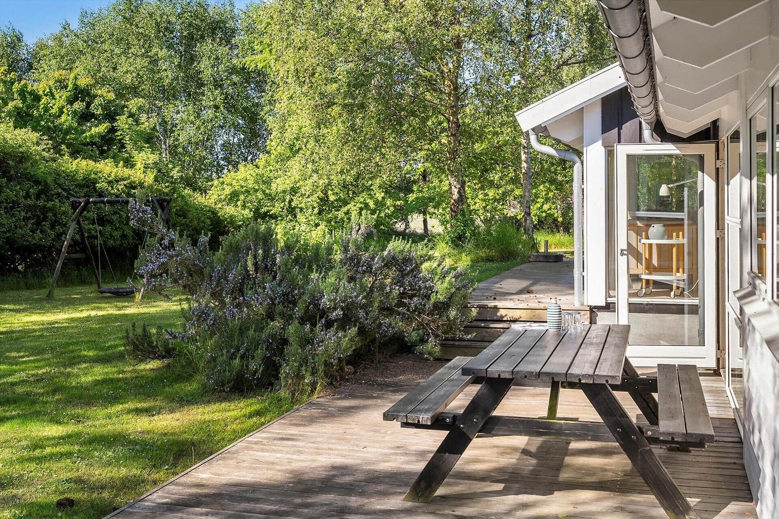 Holzterrasse mit Picknicktisch, Garten mit Schaukel und Sträuchern neben Haus