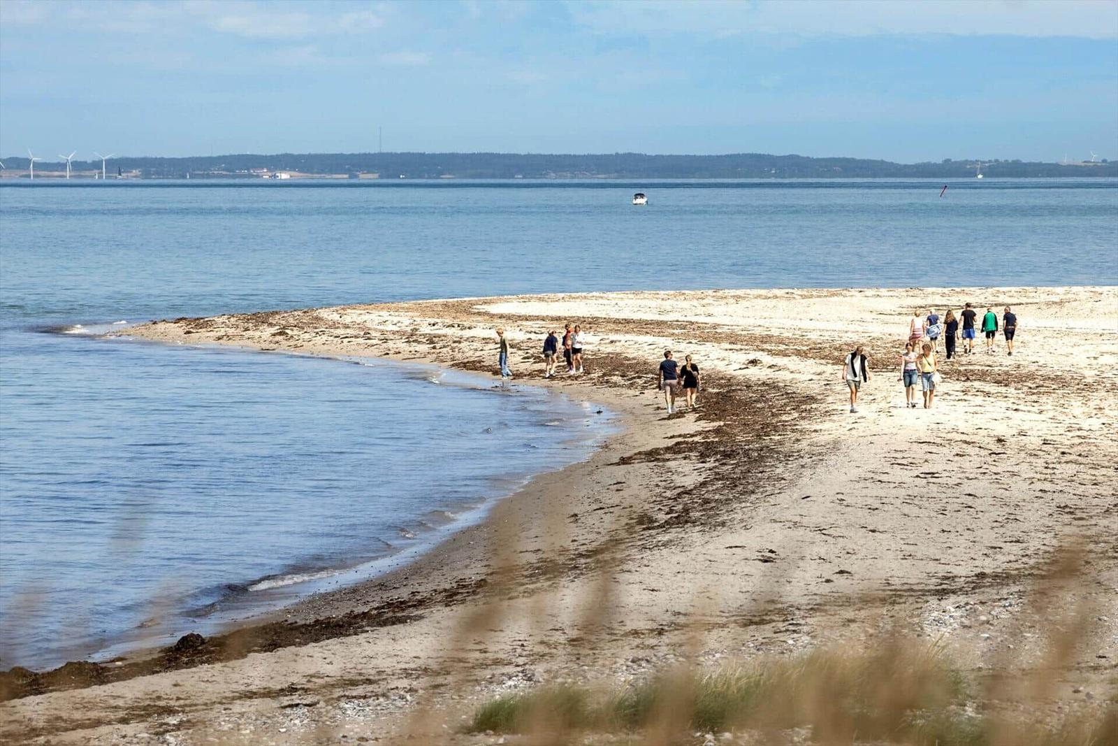 Strand mit Wanderern, ruhige See und Windkraftanlagen im Hintergrund.