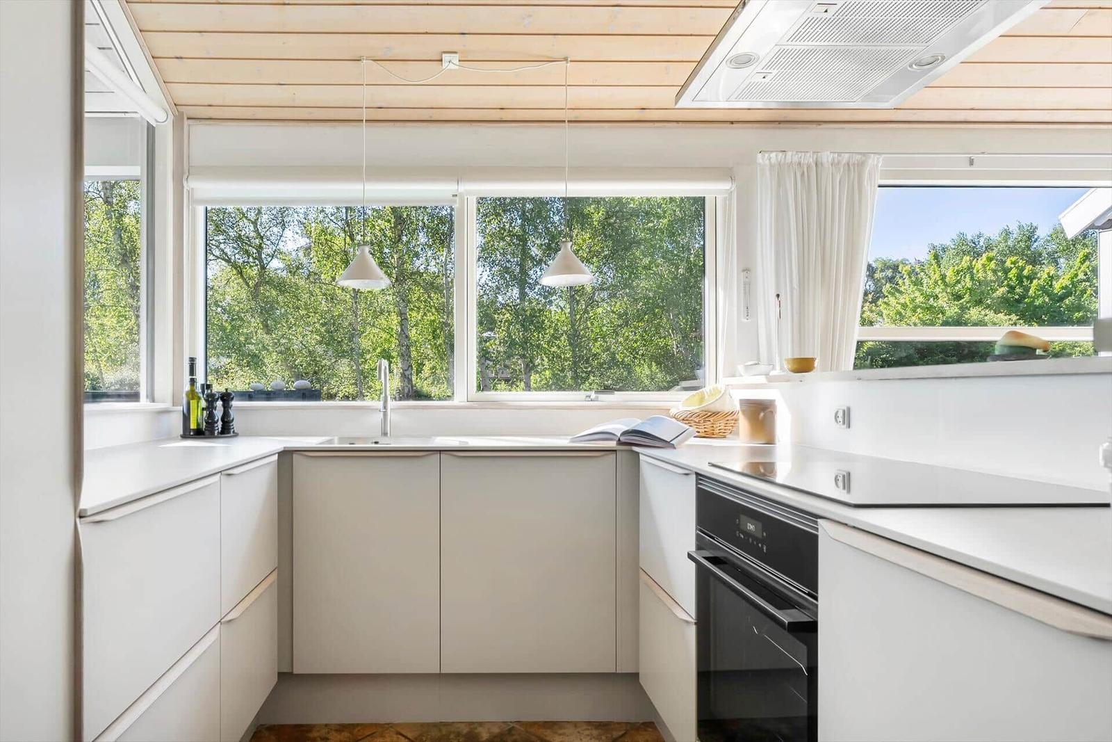 Küche mit weißen Schränken und Fenstern zum Garten