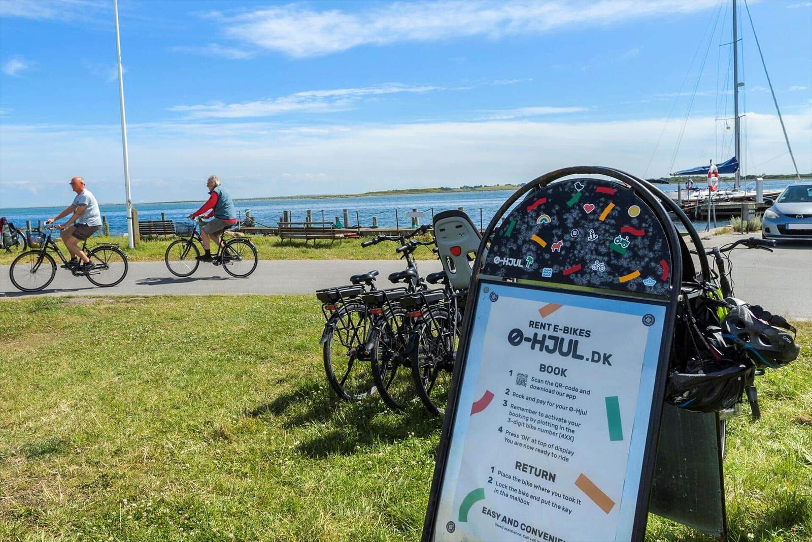 E-Bikes stehen bereit am Wasserufer mit Fahrradweg und Segelyacht im Hintergrund.