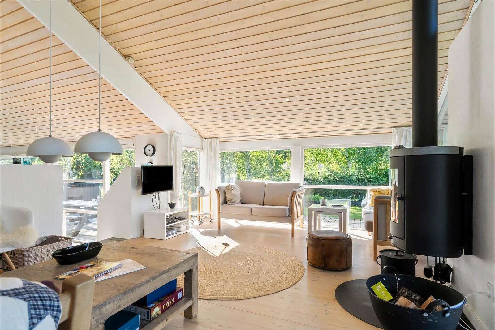 Wohnraum mit Holzdecke, Sofa, Kamin und großen Fenstern.