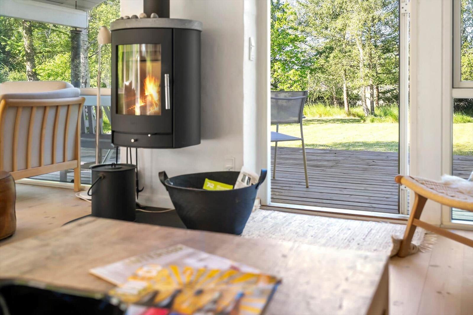 Wohnzimmer mit Kamin, Holzterrasse und Blick auf Grünflächen.