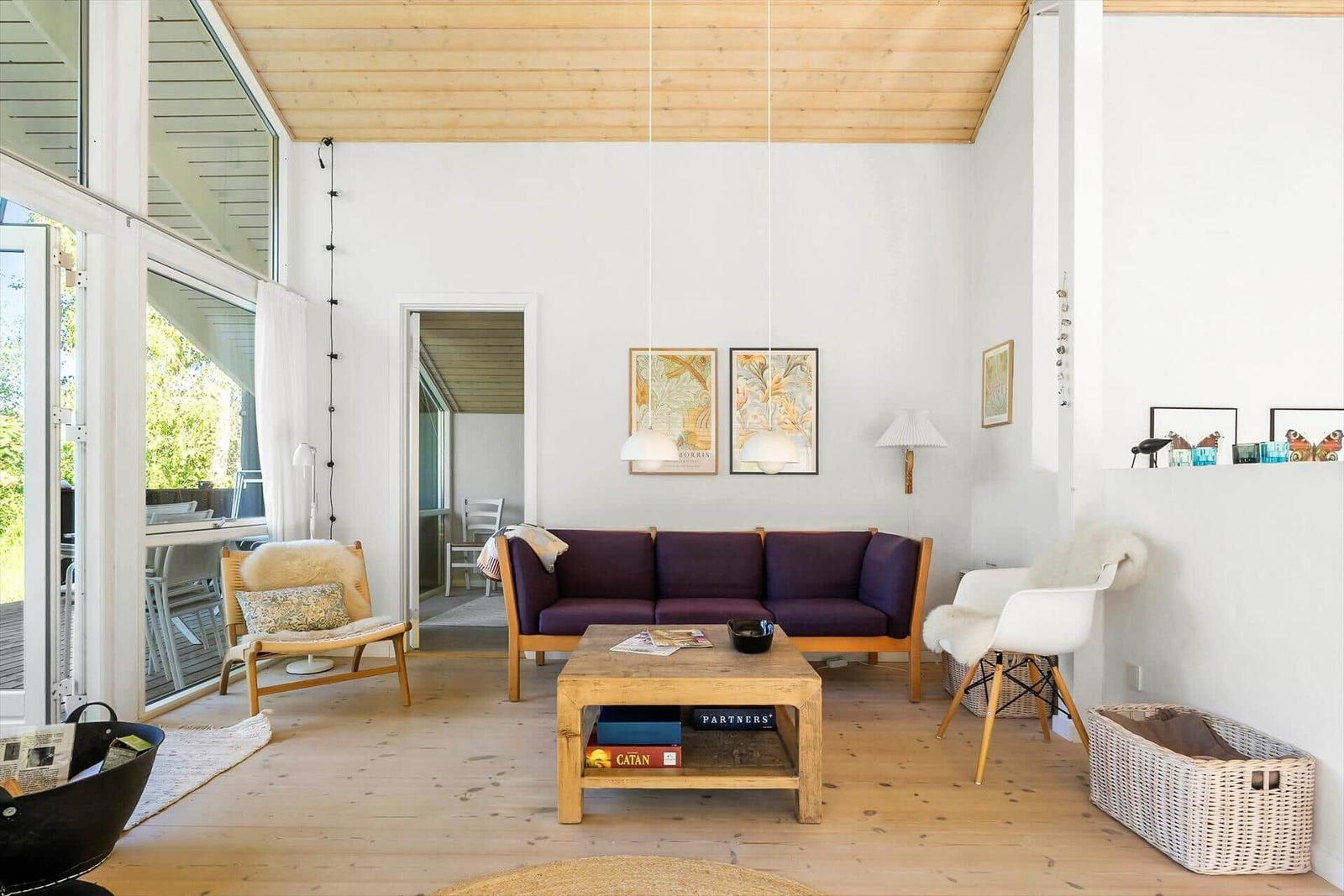 Wohnzimmer mit Sofa, Tisch und Sesseln. Holzdecke und Fenster zur Terrasse.