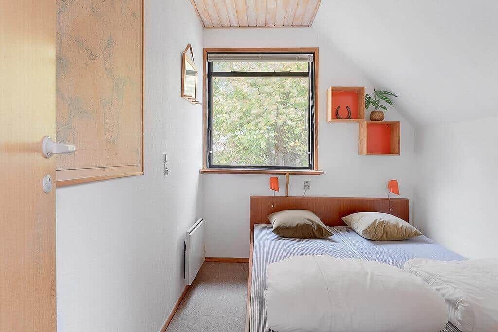 Schlafzimmer mit Dachschrägen, Fenster und Bett mit Kissen.