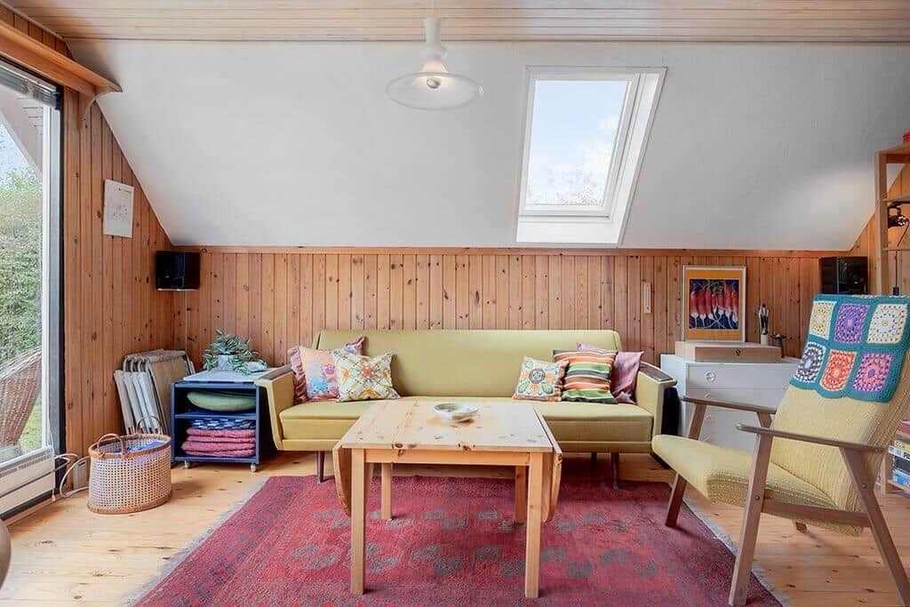 Wohnzimmer mit Sofa, Tisch und Sessel unter Dachschräge mit Fenster.