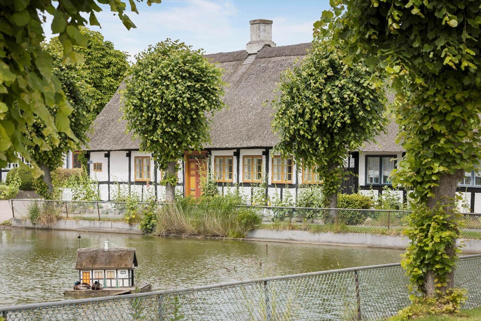 Haus mit Strohdach und Holzrahmen am Wasser mit kleinen Boot.