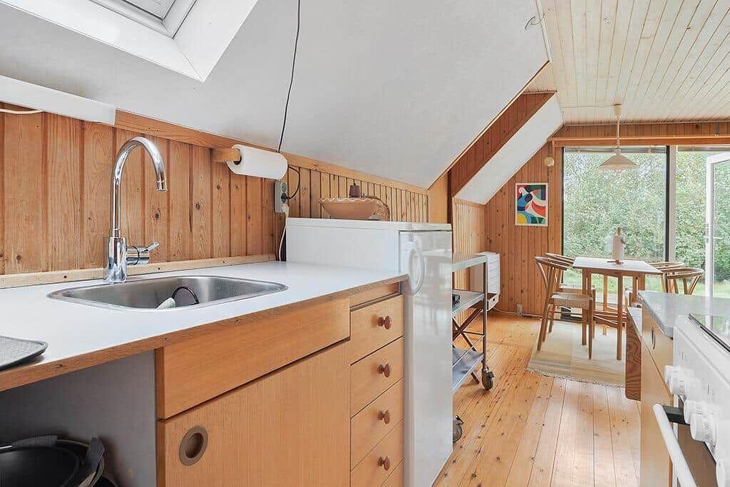 Küche mit Holzwand, Edelstahlspüle und Essbereich mit Tisch und Stühlen.