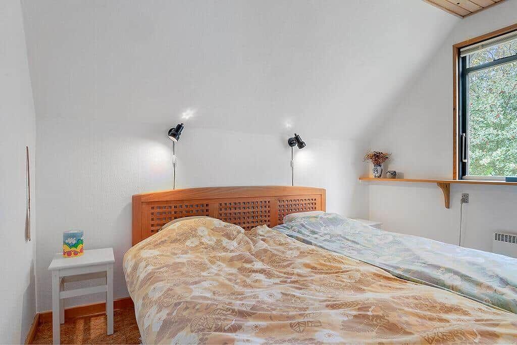 Schlafzimmer mit Holzbett, Fenster und Nachttisch.