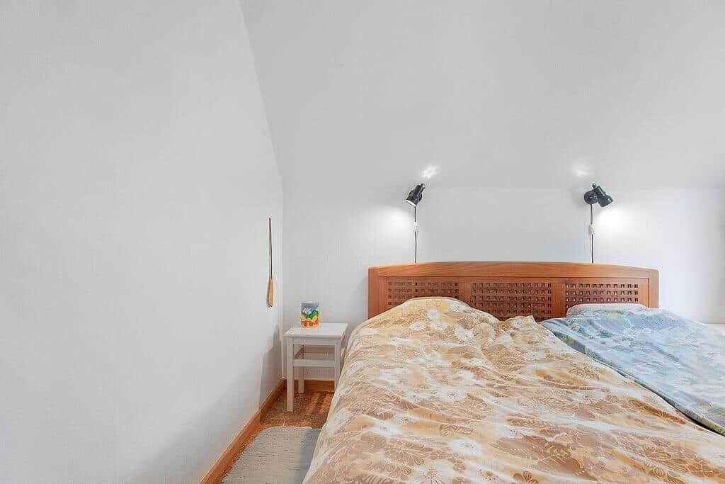 Schlafzimmer mit Holzbett, Nachttisch und Wandlampen.