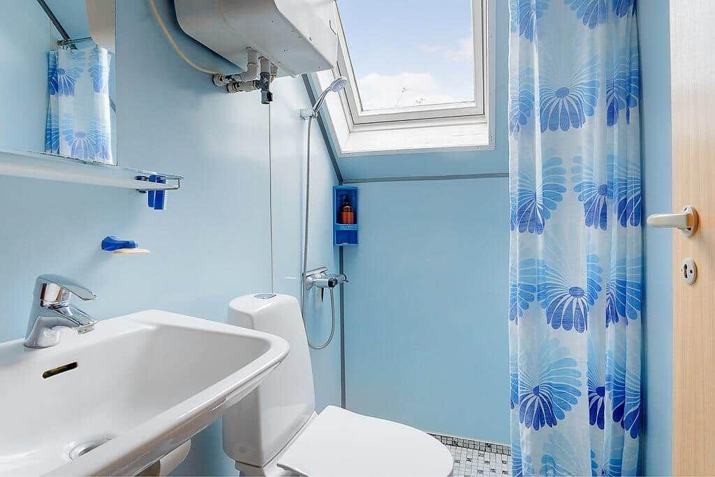 Badezimmer mit Dusche, Toilette und Waschbecken unter Dachfenster.